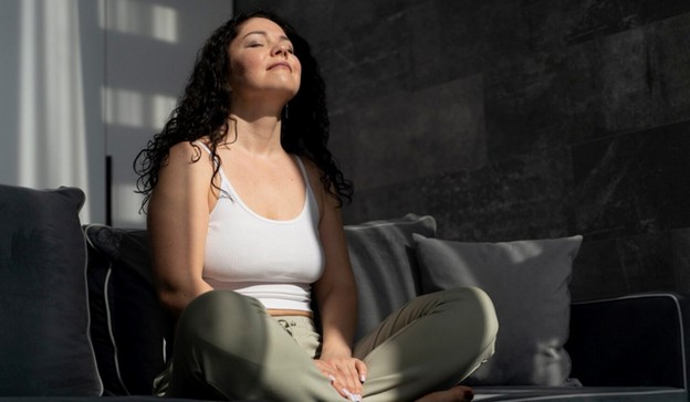 Young woman meditating on a sofa in natural sunlight 
