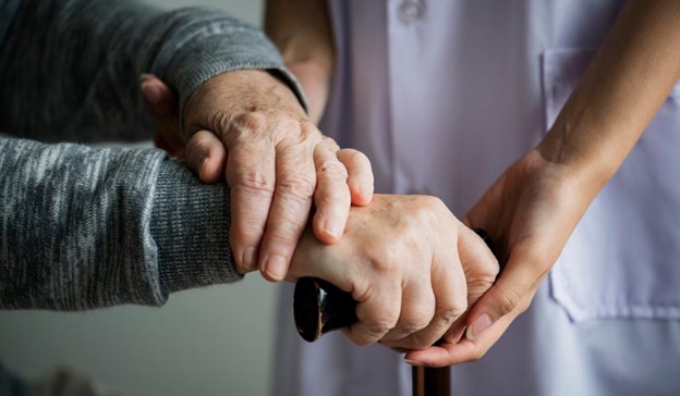 ALT Text: Caregiver holding elderly person's hand on a walking cane